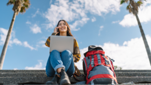 Freelancer works outdoors with a backpack sitting next to her. 