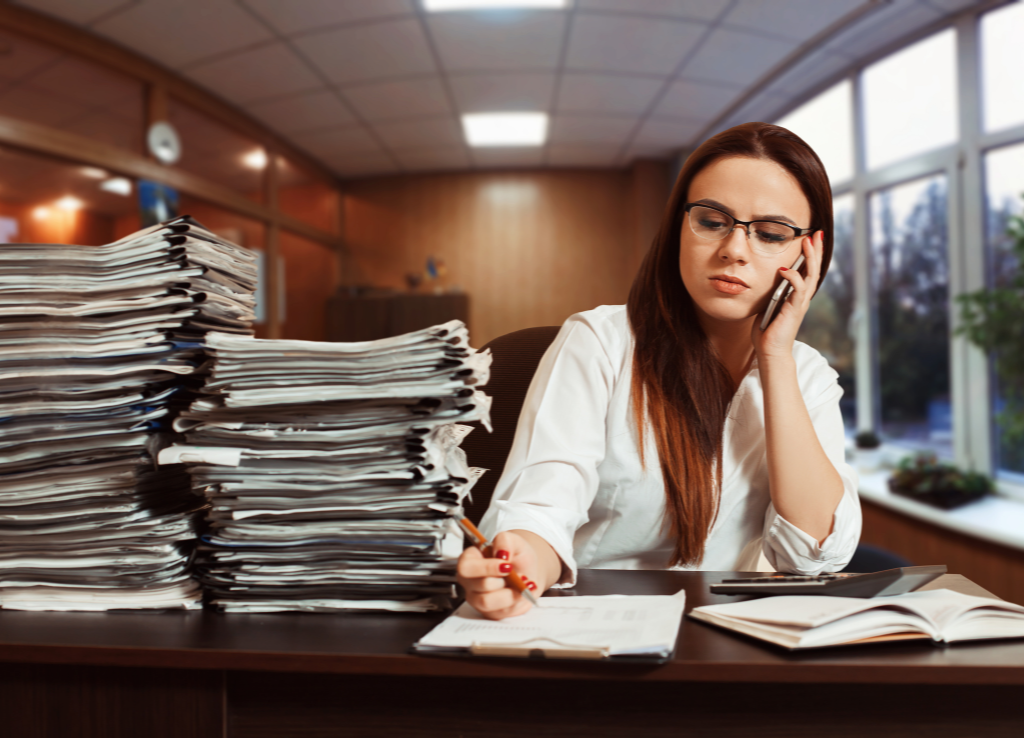 Female businesswoman sits next to a large stack of accounting paperwork
