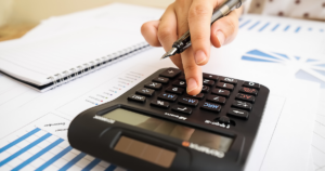 Small business owner doing bookkeeping by typing on a calculator