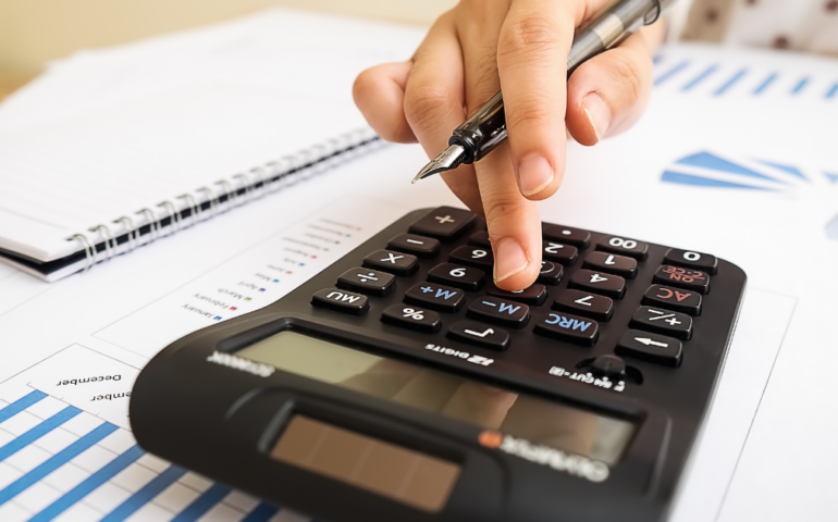 Small business owner doing bookkeeping by typing on a calculator