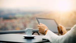 Woman holding iPad while drinking coffee overlooking a city at dawn