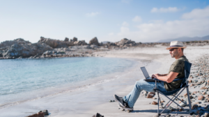 Digital nomad sits on a beach working on a laptop